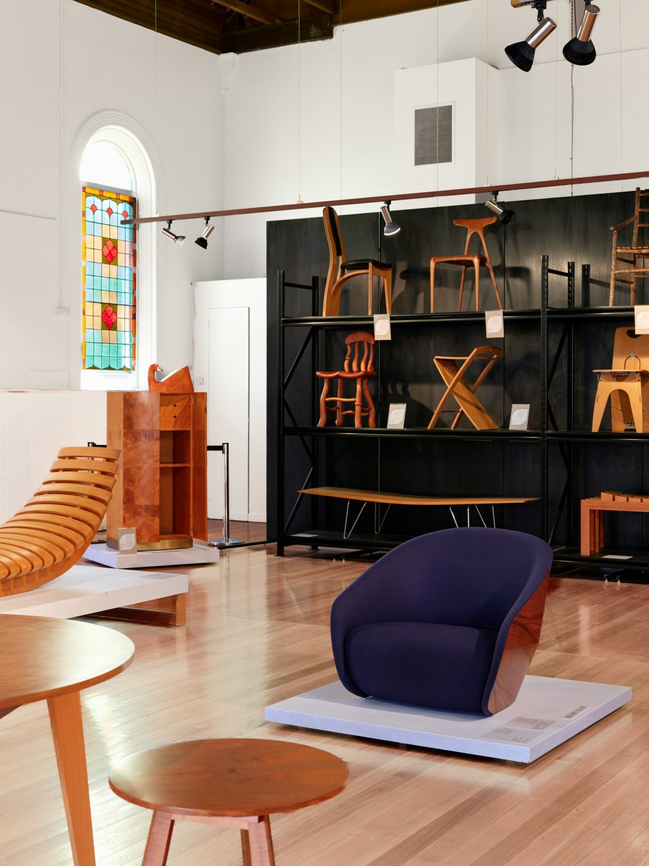 Sala espositiva con una collezione di sedute e arredi in legno, e una poltrona blu in primo piano