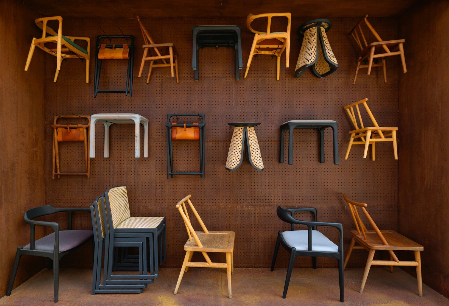 Allestimento fieristico con sedute e sgabelli di design appesi a una parete color ruggine